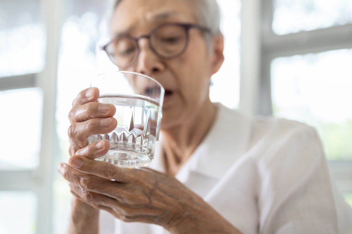 Ältere Frau hält zittrig ein Wasserglas